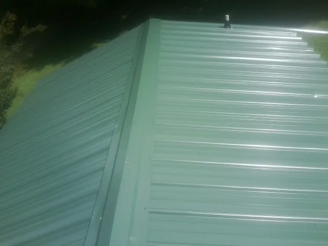 New green metal panels meeting at the ridge of a roof — Flat Roof Repair work by our crew in Parker